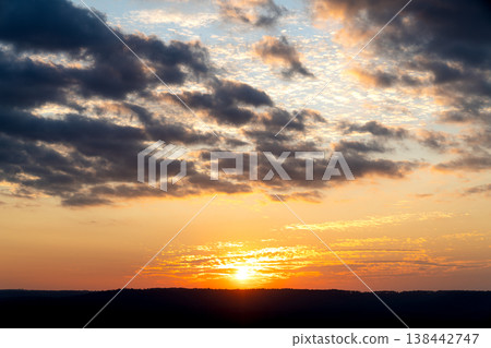 Dramatic evening sky with vibrant orange and gold sunset over dark horizon. Heavy blue and grey clouds creating beautiful contrast. Perfect for nature, travel, and weather background themes. Scenic. Dramatic evening sky with vibrant orange and gold sunset over dark horizon. Heavy blue and grey clouds creating beautiful contrast. Perfect for nature, travel, and weather background themes. Scenic. 138442747