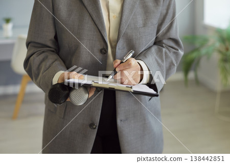 Reporter writing notes on clipboard, microphones ready for business interview Reporter writing notes on clipboard, microphones ready for business interview 138442851