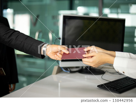 Close-up of businessperson handing passport to officer at service counter for identity verification, document control and security check in modern office, illustrating compliance and travel process 138442956