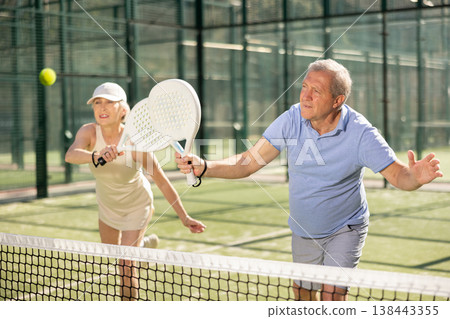 Motivated senior man and woman playing padel with his teammate in court 138443355