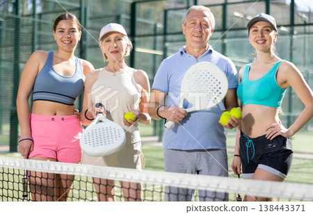 A group of tennis players posing next to the net holding Padel rackets A group of tennis players posing next to the net holding Padel rackets 138443371