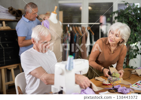 Elderly men and women spending time sewing in workroom Elderly men and women spending time sewing in workroom 138443372