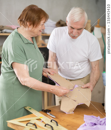 Elderly man and woman discussing pattern during sewing lesson Elderly man and woman discussing pattern during sewing lesson 138443410