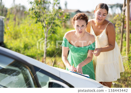 Adult and young woman signing document on car Adult and young woman signing document on car 138443442