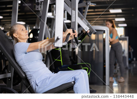 Focused mature female athlete using chest press machine in gym 138443448