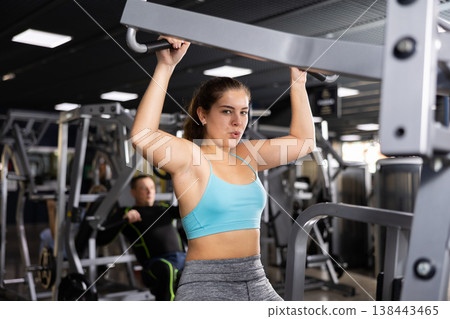 Girl training back muscles in lat pull-down lever machine 138443465