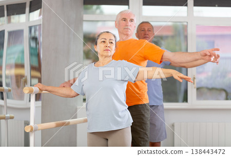 Close-up view of mature woman practicing ballet positions standing by ballet-barre Close-up view of mature woman practicing ballet positions standing by ballet-barre 138443472