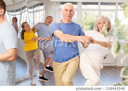 Enthusiastic senior couple practicing jive in group dance class 138443540