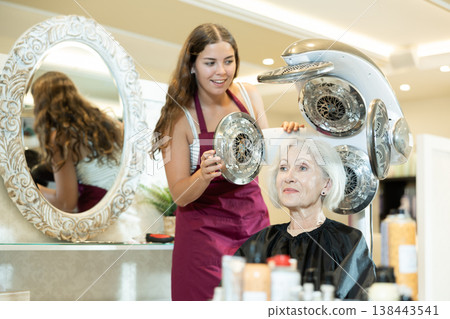 Young female hairdresser adjusting settings of thermostimulator for elderly woman Young female hairdresser adjusting settings of thermostimulator for elderly woman 138443541