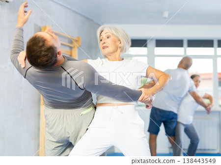 Senior woman in pair with middle-aged coach train Krav Maga and self-defense skills. Senior woman in pair with middle-aged coach train Krav Maga and self-defense skills. 138443549