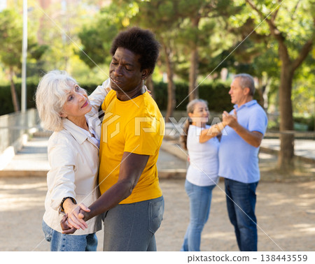 Carefree senior multiracial couples dancing in pairs outdoors during sunny day at park 138443559