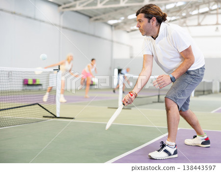 Sporty man pickleball tennis player trains on the indoor court using a racket to hit ball Sporty man pickleball tennis player trains on the indoor court using a racket to hit ball 138443597
