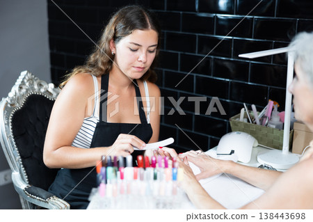 Skilled woman manicurist filing and shaping nails of female client during procedure of manicure in beauty salon Skilled woman manicurist filing and shaping nails of female client during procedure of manicure in beauty salon 138443698