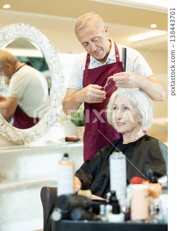 Experienced senior man master makes performs haircut for mature woman with scissors Experienced senior man master makes performs haircut for mature woman with scissors 138443701