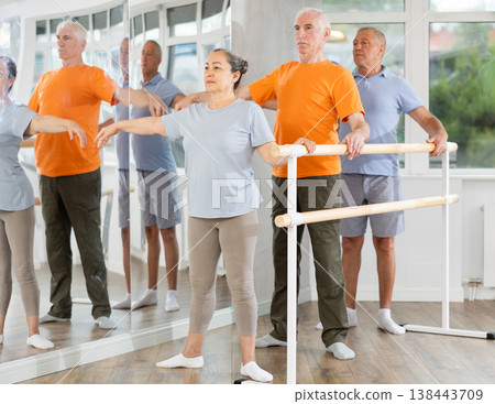 Active mature woman practicing second position holding by ballet barre together with others 138443709