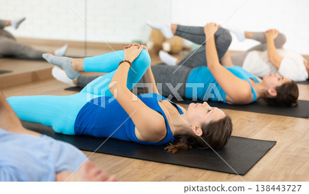 Acitve male and female of different ages lying on mats during Pilates stretching training in fitness studio Acitve male and female of different ages lying on mats during Pilates stretching training in fitness studio 138443727