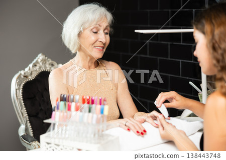 Unrecognizable girl manicure master files nails and performs grooming procedure for senior woman 138443748