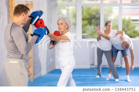 Old woman training boxing kicks on punch mitts held by instructor Old woman training boxing kicks on punch mitts held by instructor 138443751