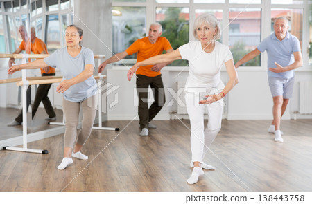Confident senior woman training ballet moves with group of older people at ballet school Confident senior woman training ballet moves with group of older people at ballet school 138443758