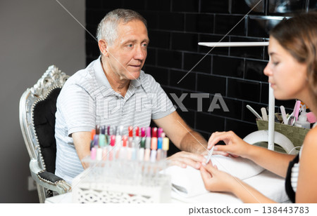 Blurry manicurist girl works with elderly male client, files nails and performs hand care procedure Blurry manicurist girl works with elderly male client, files nails and performs hand care procedure 138443783