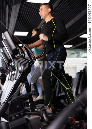 Strong sportsman training at elliptical machine in gym Strong sportsman training at elliptical machine in gym 138443797