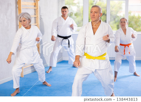 Old man attendee of karate classes practicing kata standing in row with others Old man attendee of karate classes practicing kata standing in row with others 138443813