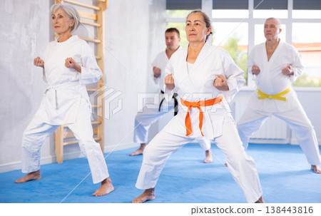 Old woman attendee of karate classes practicing kata standing in row with others 138443816