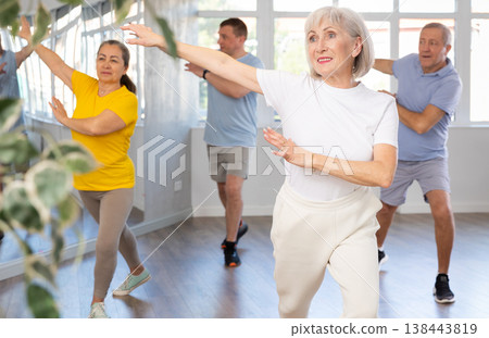 Elderly woman practicing Tai Chi with group in training room Elderly woman practicing Tai Chi with group in training room 138443819
