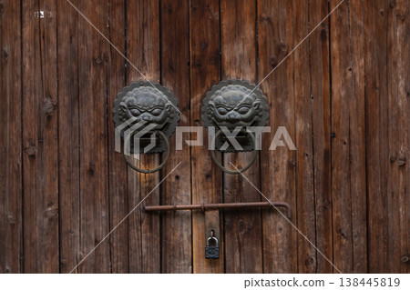Traditional Chinese door knockers mounted on a weathered wooden door Traditional Chinese door knockers mounted on a weathered wooden door 138445819