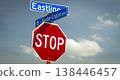Red octagonal stop sign mounted beneath blue street signs at an intersection against a bright blue sky with fluffy clouds, conveying traffic control, safety, direction and urban signage 138446457