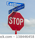 Red octagonal stop sign mounted beneath blue street signs at an intersection against a bright blue sky with fluffy clouds, conveying traffic control, safety, direction and urban signage 138446458