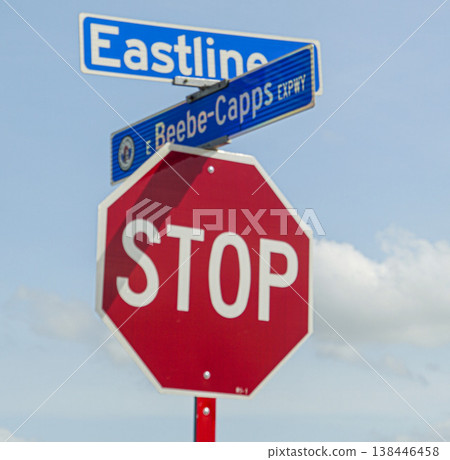 Red octagonal stop sign mounted beneath blue street signs at an intersection against a bright blue sky with fluffy clouds, conveying traffic control, safety, direction and urban signage Red octagonal stop sign mounted beneath blue street signs at an intersection against a bright blue sky with fluffy clouds, conveying traffic control, safety, direction and urban signage 138446458