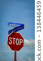 Red octagonal stop sign mounted beneath blue street signs at an intersection against a bright blue sky with fluffy clouds, conveying traffic control, safety, direction and urban signage 138446459