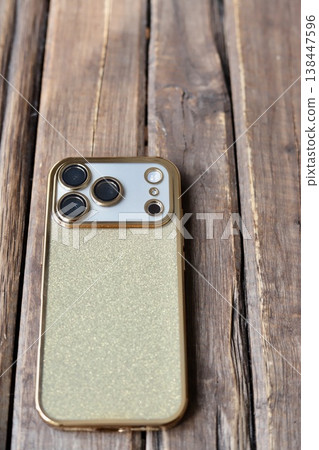 A triple-camera smartphone with a gold glitter back case. 138447596