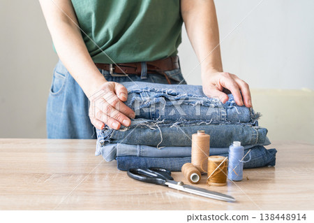 Person preparing upcycled denim fabric, thread, and scissors for sewing. Creative craft hobby saving the environment, upcycling denim jeans reusing old clothes. Reusing things Person preparing upcycled denim fabric, thread, and scissors for sewing. Creative craft hobby saving the environment, upcycling denim jeans reusing old clothes. Reusing things 138448914