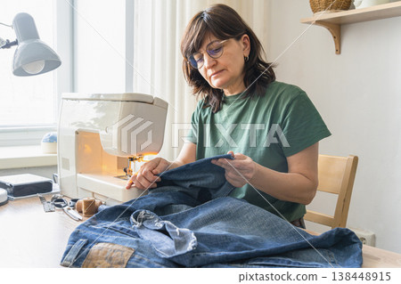 An adult woman using a domestic sewing machine, stitching denim fabric for clothing repair. Demonstrating hobby craft and design work 138448915