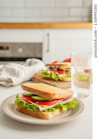 Two club sandwiches with ham, cheese, tomatoes, lettuce, cucumber on a plate on white kitchen table Two club sandwiches with ham, cheese, tomatoes, lettuce, cucumber on a plate on white kitchen table 138449160