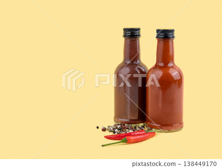 Two spicy sauce bottles with chili peppers and spices on yellow background. Two spicy sauce bottles with chili peppers and spices on yellow background. 138449170