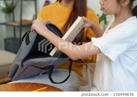 Child placing a book into a school backpack 138449636