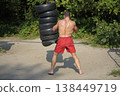 Muscular boxer training outdoors hitting heavy punching bag made of car tires in the park 138449719