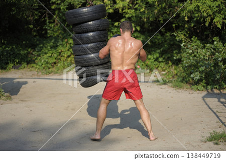 Muscular boxer training outdoors hitting heavy punching bag made of car tires in the park Muscular boxer training outdoors hitting heavy punching bag made of car tires in the park 138449719