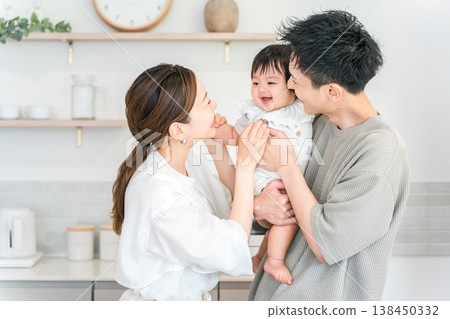 A couple and family holding their baby in the kitchen. 138450332
