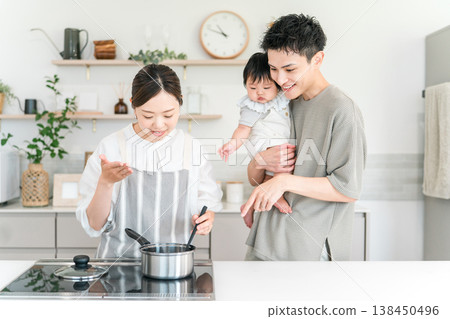 一位父親抱著嬰兒在廚房裡,一位母親圍著圍裙,一家人其樂融。 一位父親抱著嬰兒在廚房裡,一位母親圍著圍裙,一家人其樂融。 138450496