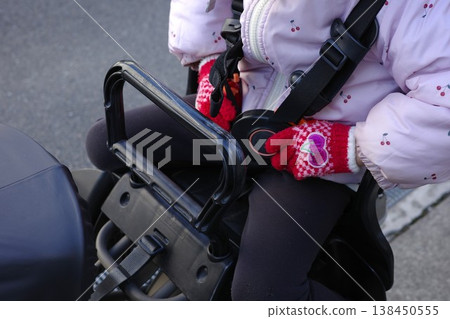 A little girl wearing red gloves tries to fasten the seatbelt on her bicycle child seat. A little girl wearing red gloves tries to fasten the seatbelt on her bicycle child seat. 138450555
