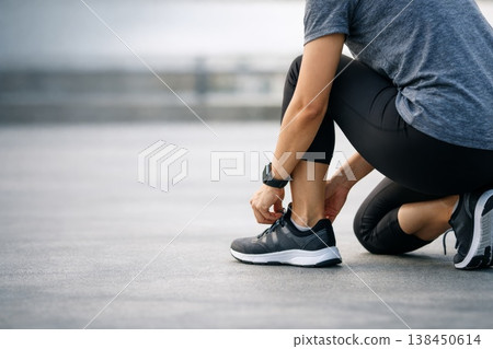 Runner Getting Ready At Bridge. Training Athlete Adjusting Shoelaces At Waterway. Dedicated Runner Preparing Shoes For Workout Beneath City Bridge With Concentration 138450614
