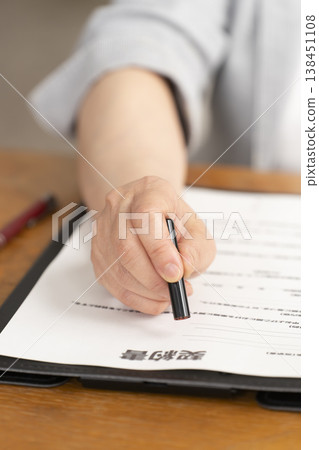 一位老婦人在合約上簽字蓋章時的手。 一位老婦人在合約上簽字蓋章時的手。 138451108