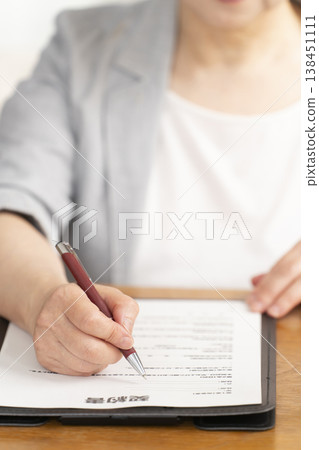 一位老婦人在合約上簽字蓋章時的手。 一位老婦人在合約上簽字蓋章時的手。 138451111