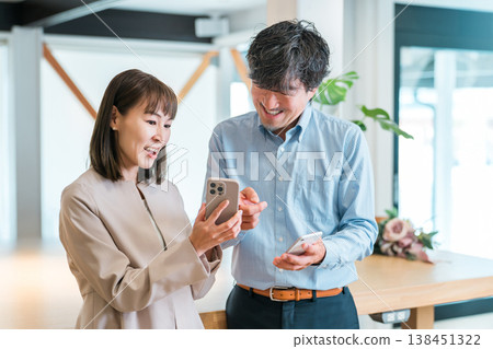 Businesswoman and businessman looking at smartphone in office (IT company employee) Businesswoman and businessman looking at smartphone in office (IT company employee) 138451322