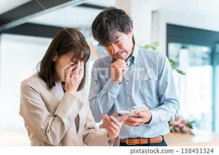 Businessman and businesswoman talking while looking at smartphone (worried, troubled, stressed, trouble) 138451324