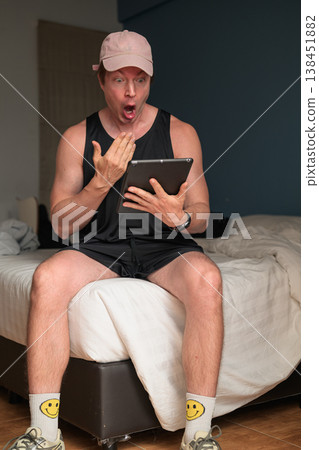 Shocked Caucasian Man with Tablet on Bed in Minimalist Bedroom with Copy Space Shocked Caucasian Man with Tablet on Bed in Minimalist Bedroom with Copy Space 138451882